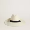 Gouden fedora hoed van wit stro met zwart lint en maritieme print onder de rand.