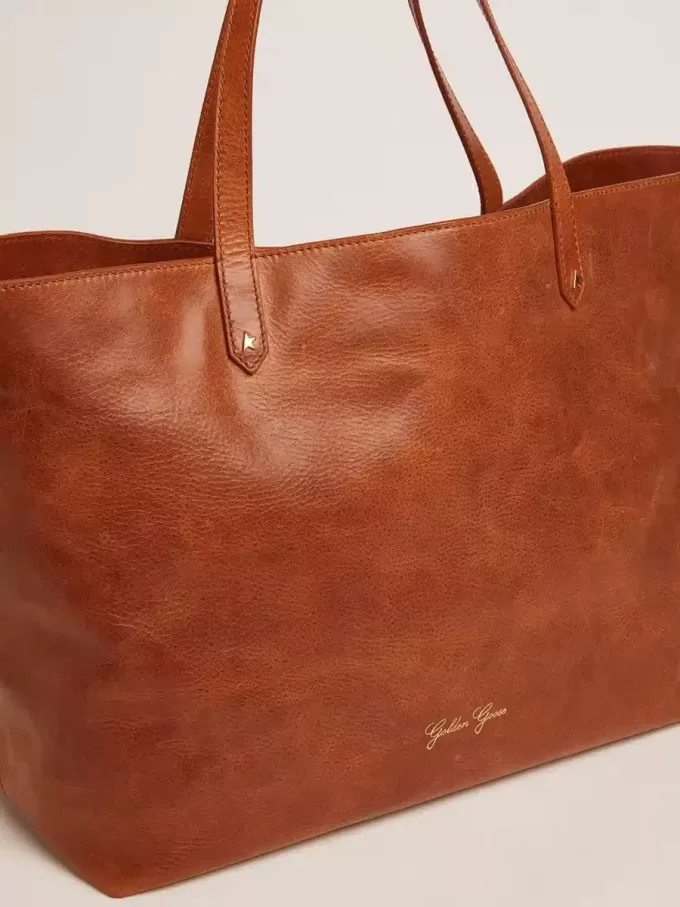 Pasadena-tas in glanzend, gehamerd leer in tan-kleur met gouden logo op de voorkant